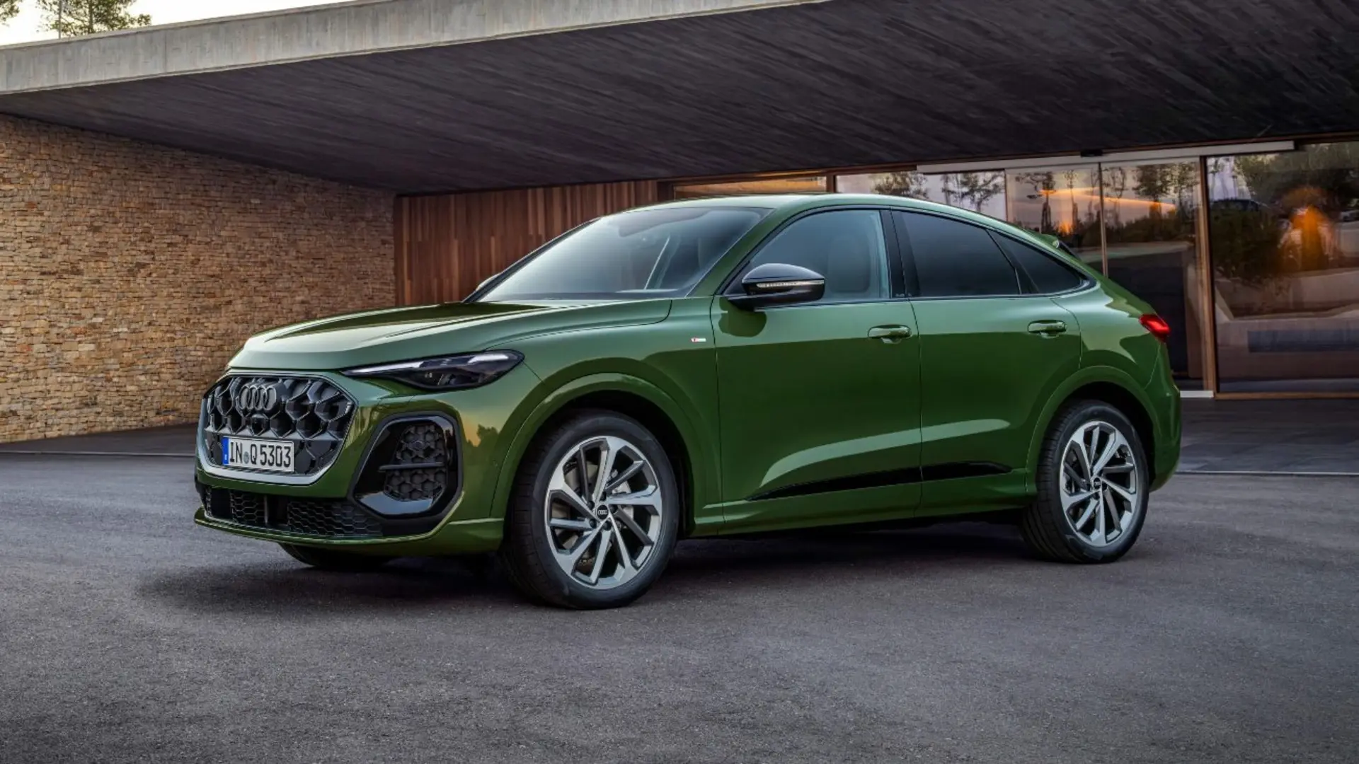 نمای نیم‌رخ از خودروی شاسی‌بلند سبز رنگ آئودی مدل Q5 Sportback در مقابل یک ساختمان مدرن