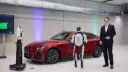 ربات انسان‌نمای هوشمند در کنار خودروی قرمز برند بی‌ام‌و (BMW)