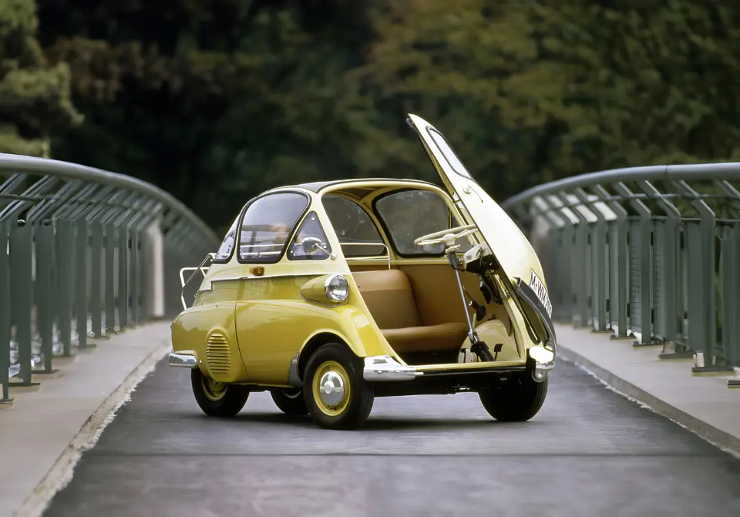 خودروی کوچک زرد رنگ ایزتا (Isetta) با در جلوی باز شده در مسیر پیاده‌رو