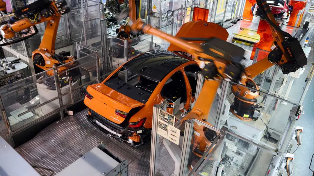 خودروی نارنجی در خط مونتاژ اتوماتیک با بازوهای رباتیک KUKA (KUKA)