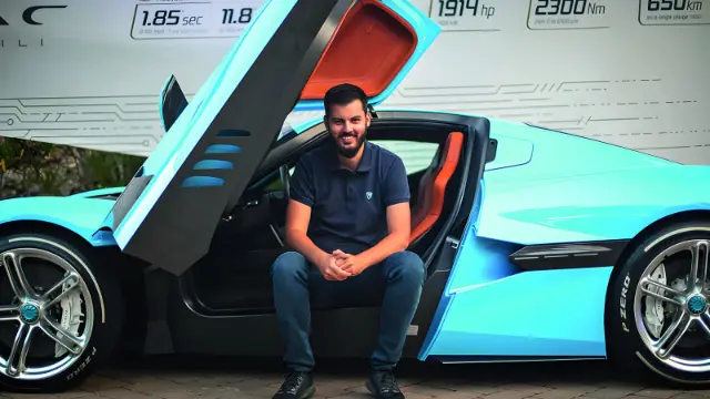 خودروی بوگاتی (Bugatti) آبی‌رنگ با درهای بال پروانه‌ای و مردی نشسته در کنار آن