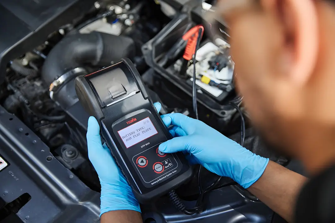 دستگاه تست باتری (Battery Tester) در حال بررسی سلامت باتری خودرو توسط تکنسین