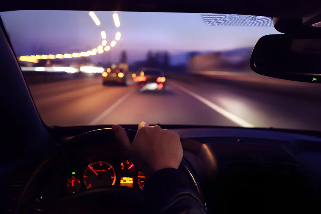نمای نزدیک از سرعت‌سنج (Speedometer) خودرو در حال حرکت در جاده در شب