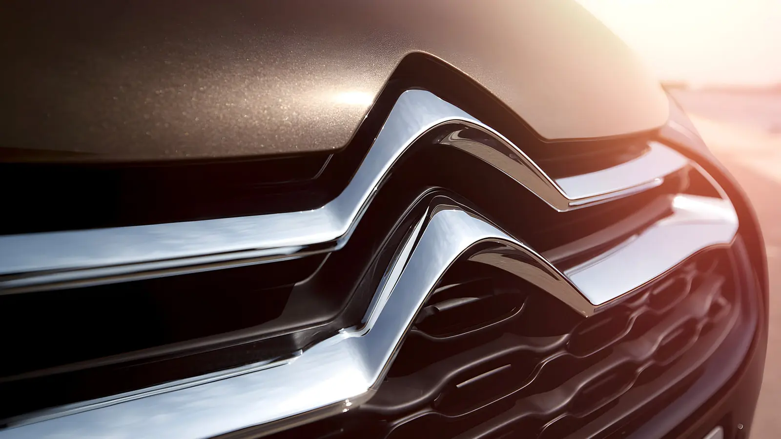 لوگوی کروم نشان سیتروئن (Citroën) روی جلوی خودروی قهوه‌ای رنگ