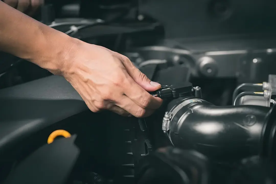 دست تعمیرکار در حال بررسی و تمیز کردن سنسور موتور خودرو
