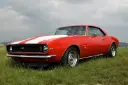 شورولت کامارو (Chevrolet Camaro) قرمز با خطوط سفید در چمنزار
