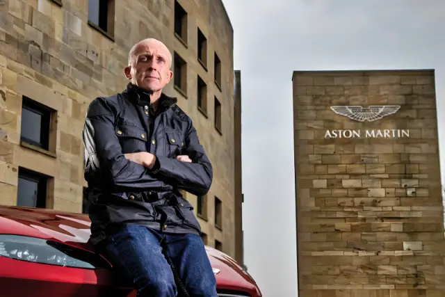کریس گودوین (Chris Goodwin) با دست‌های گره‌خورده در مقابل ساختمان استون مارتین (Aston Martin)