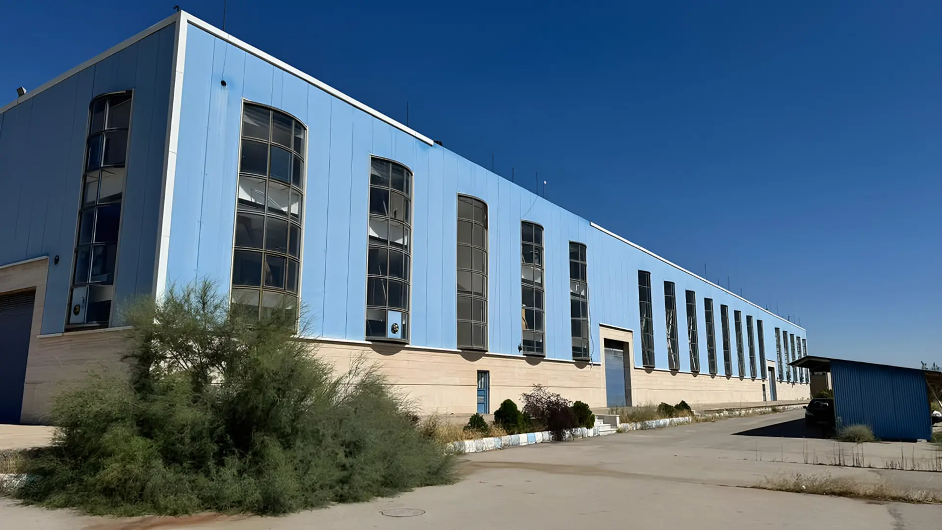 ساختمان صنعتی کارخانه سناباد خودرو توس با نمای آبی و پنجره‌های بلند