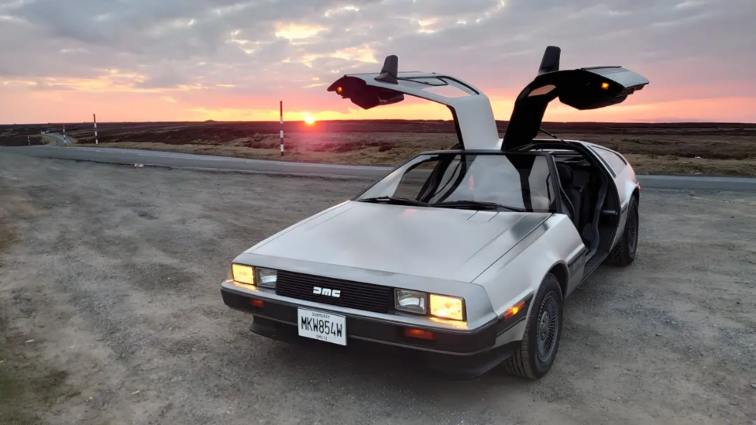 خودرو دیلورین (DeLorean) با درهای بال‌پرنده در مسیر جاده‌ای هنگام غروب