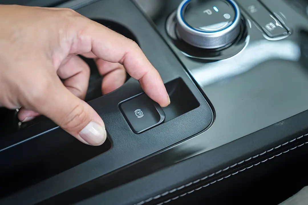 دستی که دکمه ترمز دستی الکترونیکی (Electronic Parking Brake) را در کنسول خودرو فشار می‌دهد