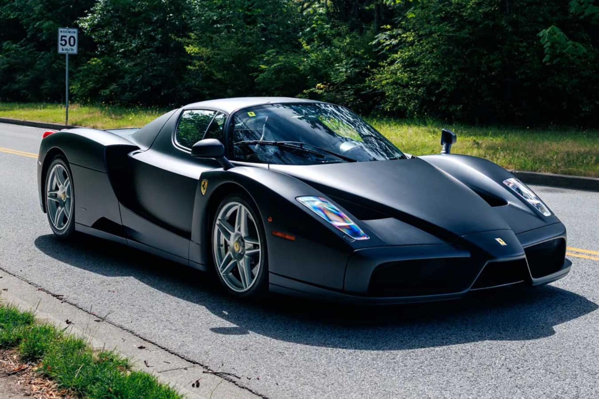فراری انزو (Ferrari Enzo) با رنگ مشکی مات در جاده‌ای میان درختان