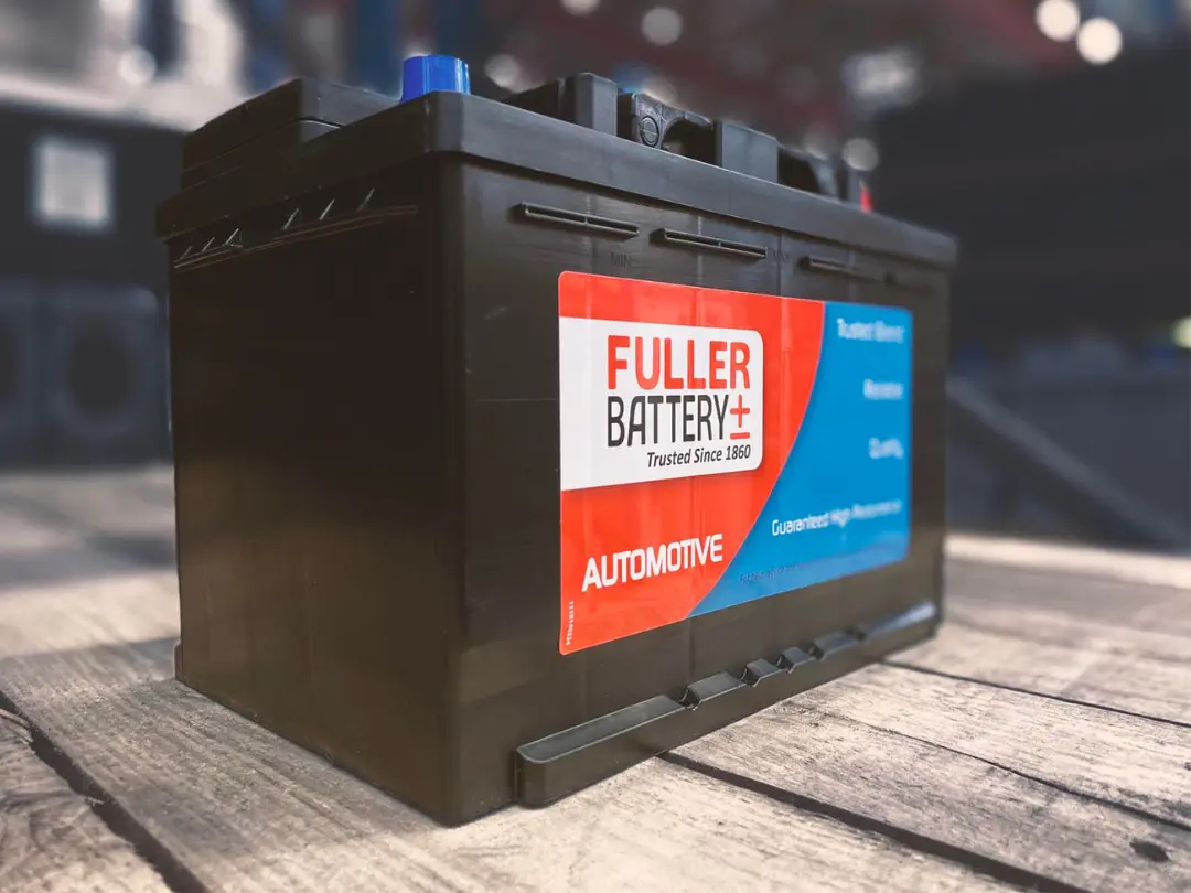 باتری خودرو مدل فولر (Fuller Battery) با برچسب قرمز و سفید روی میز چوبی