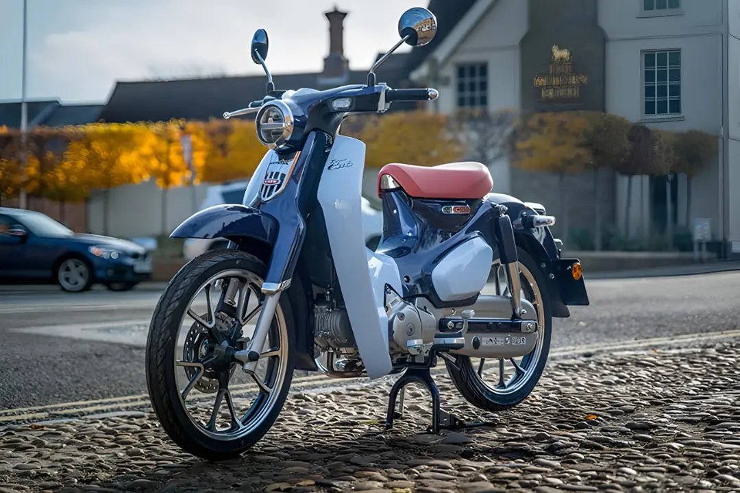 موتورسیکلت کلاسیک هوندا (Honda) با بدنه آبی و سفید روی سنگ‌فرش