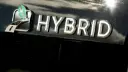 نشان فلزی کلمه HYBRID روی بدنه سیاه خودروی هیبریدی