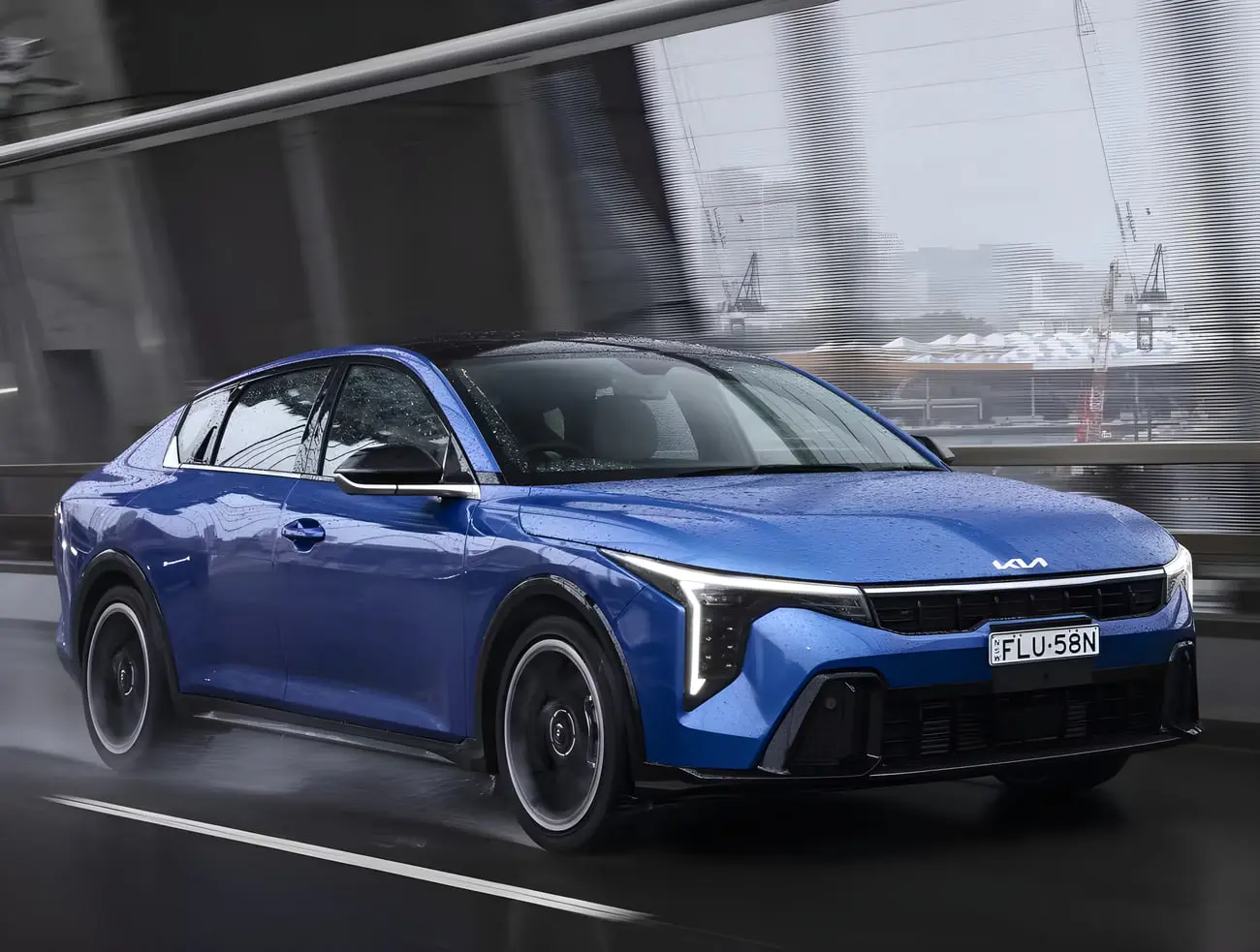سدان آبی رنگ کیا (Kia K4) در حال حرکت در جاده بارانی