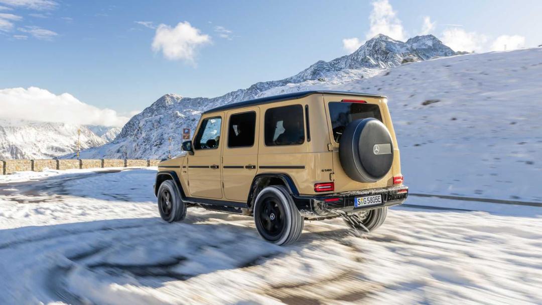 مرسدس جی‌واگن (Mercedes-Benz G-Class) طلایی‌رنگ در حال حرکت در جاده‌ای برفی میان کوه‌ها