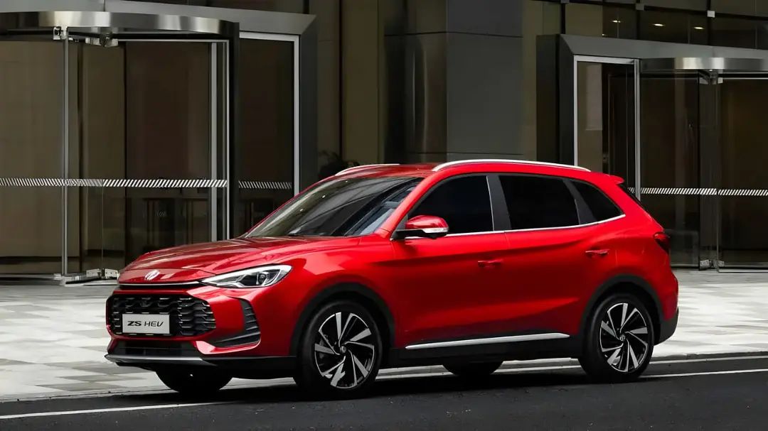 خودرو ام جی ZS هیبریدی (MG ZS HEV) قرمز رنگ در مقابل یک ساختمان مدرن