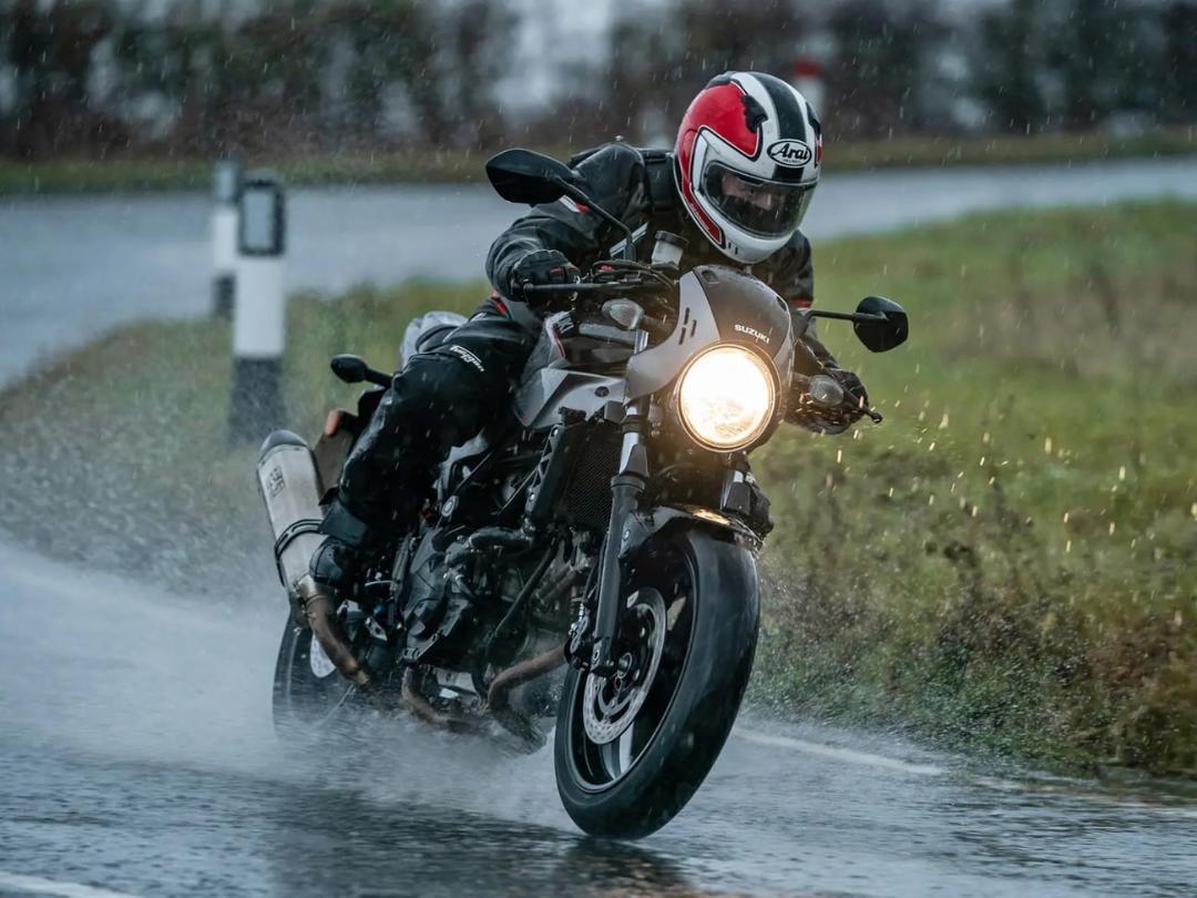 موتورسوار با کلاه ایمنی در حال رانندگی با موتور سوزوکی (Suzuki) روی جاده بارانی