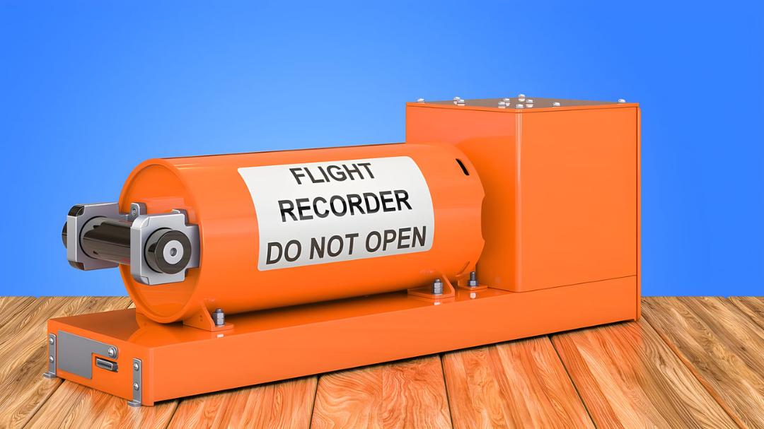 جعبه سیاه هواپیما (Flight Recorder) با بدنه نارنجی رنگ روی میز چوبی