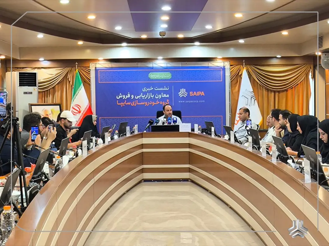 مردی در حال صحبت در یک نشست خبری رسمی با حضور خبرنگاران و بنر گروه خودروسازی سایپا