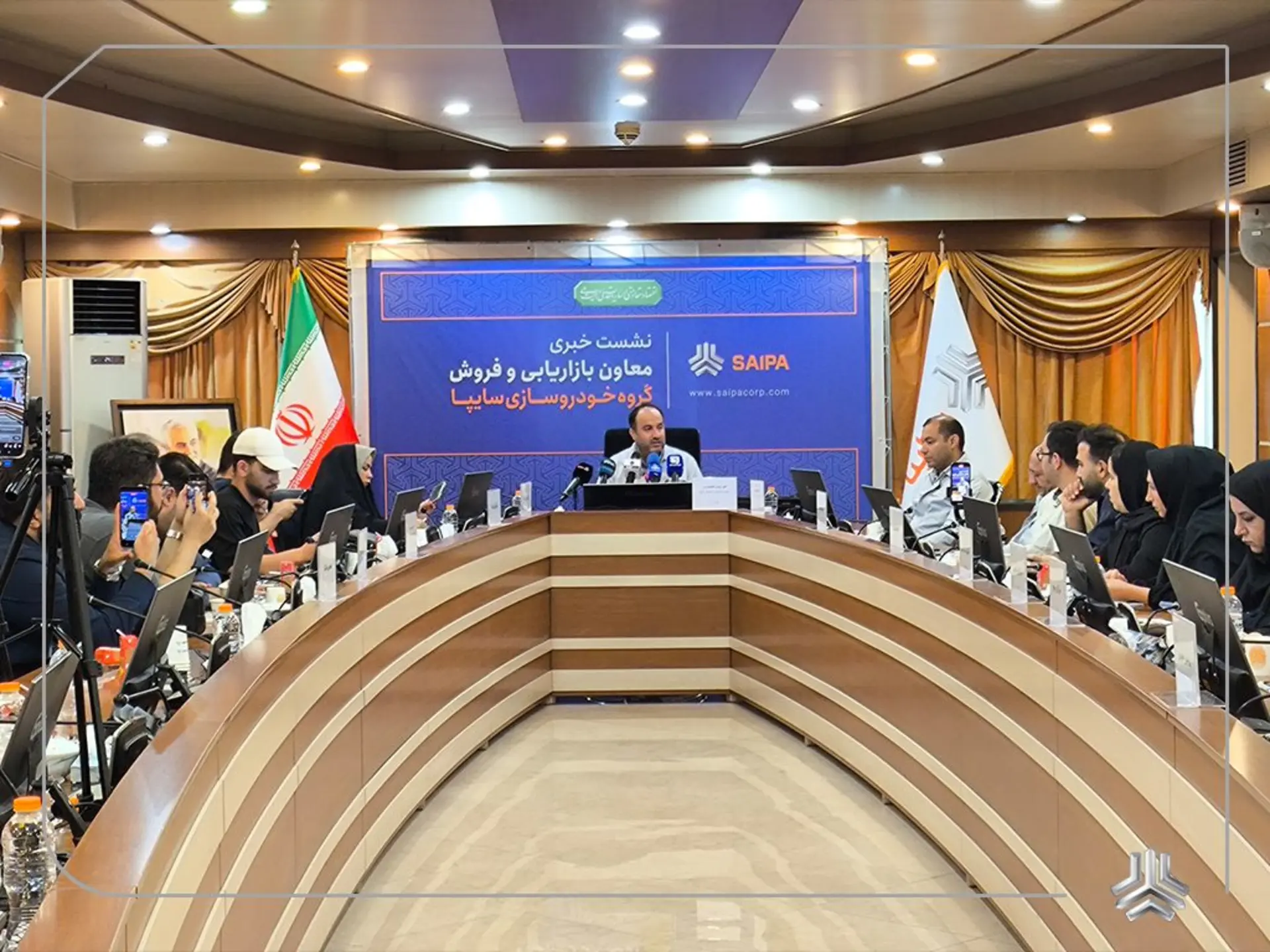 مردی در حال صحبت در یک نشست خبری رسمی با حضور خبرنگاران و بنر گروه خودروسازی سایپا