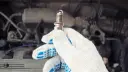 شمع موتور (Spark Plug) در دست تعمیرکار جلوی موتور خودرو