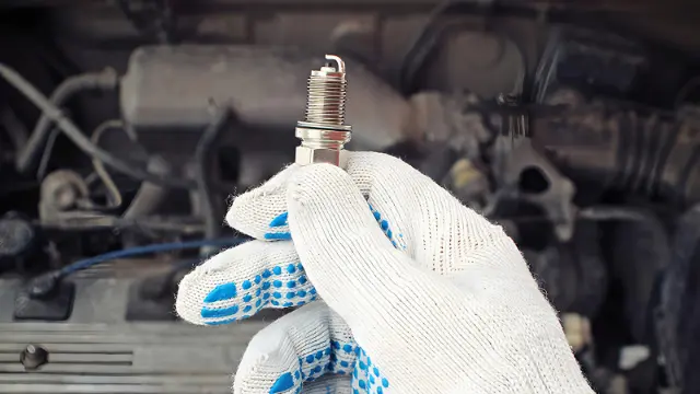 شمع موتور (Spark Plug) در دست تعمیرکار جلوی موتور خودرو