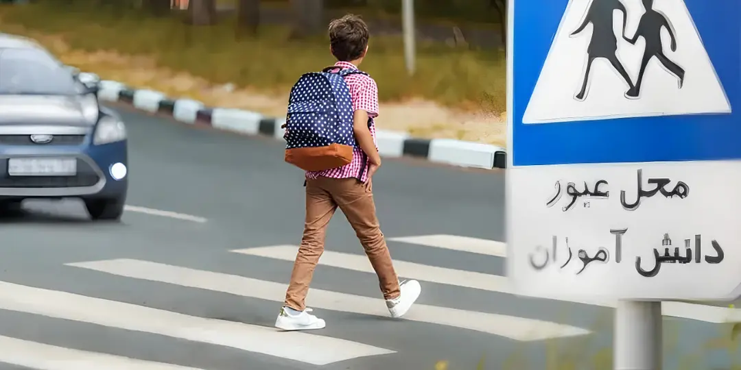 دانش‌آموز با کوله‌پشتی در حال عبور از خط پیاده‌رو در نزدیکی مدرسه