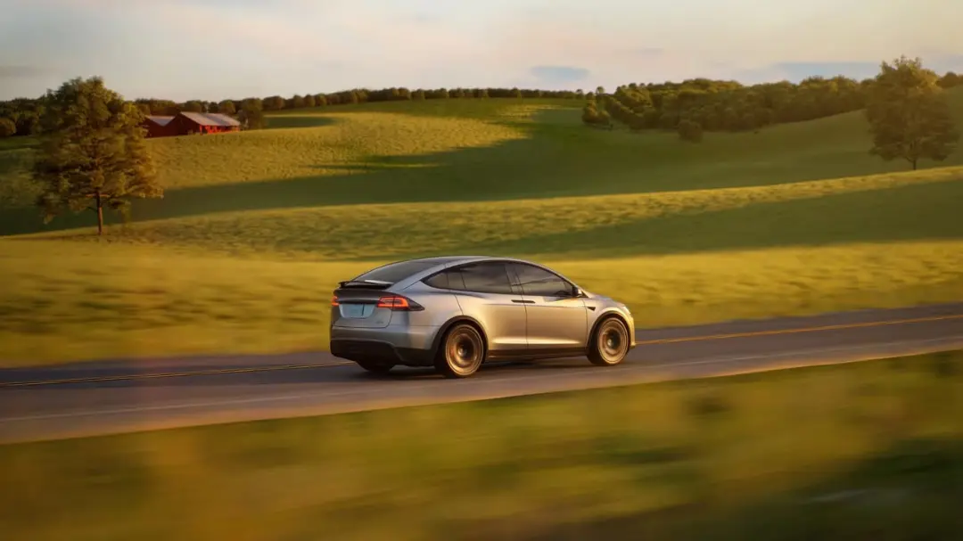 خودرو تسلا (Tesla) در حال حرکت در جاده‌ای میان تپه‌های سبز