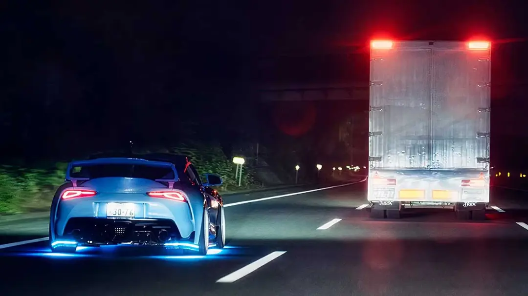 خودروی تویوتا (Toyota) در جاده شبانه در کنار یک کامیون بزرگ