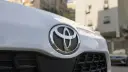 لوگوی فلزی برند تویوتا (Toyota) روی بدنه سفید خودرو