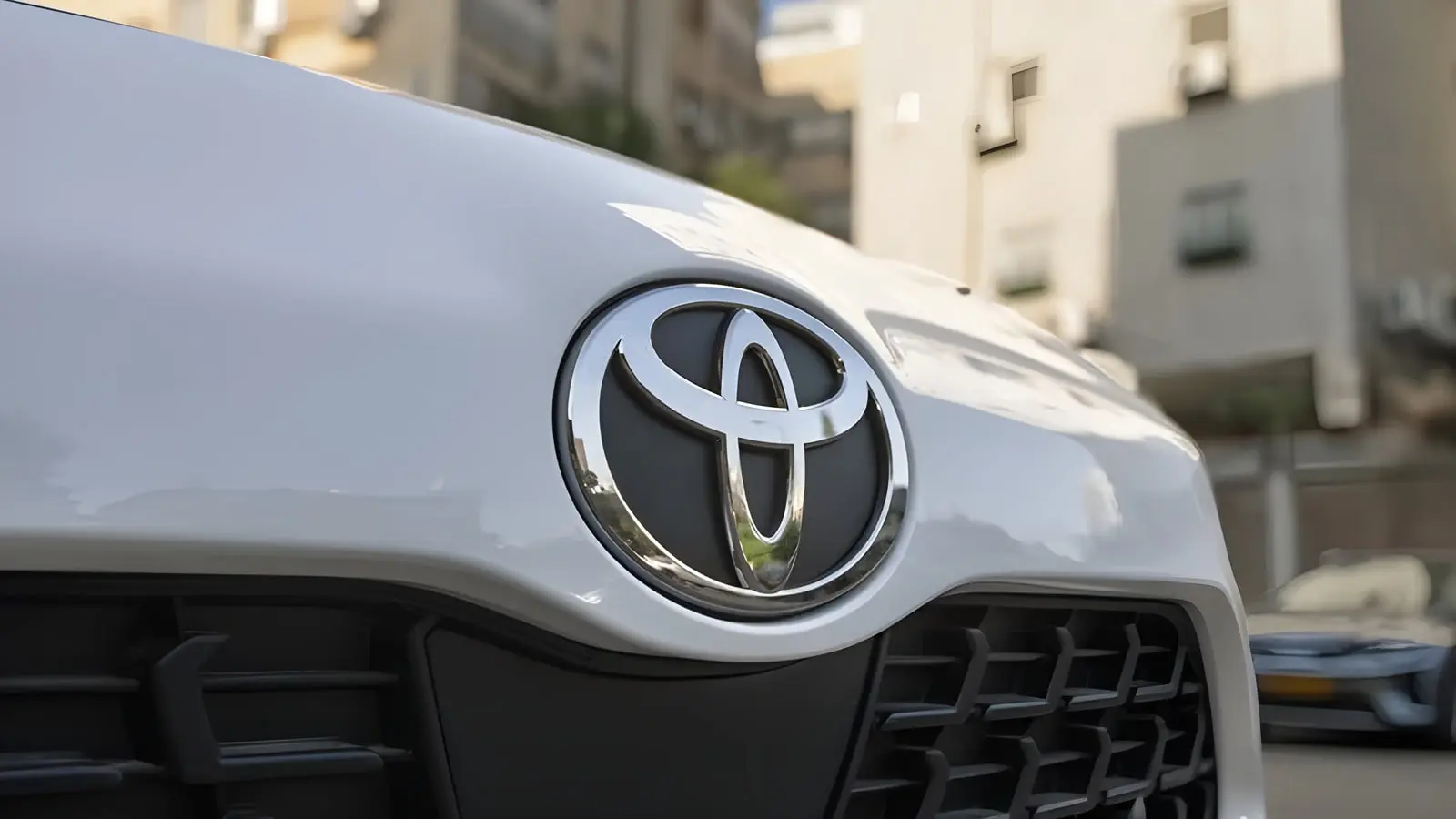 لوگوی فلزی برند تویوتا (Toyota) روی بدنه سفید خودرو
