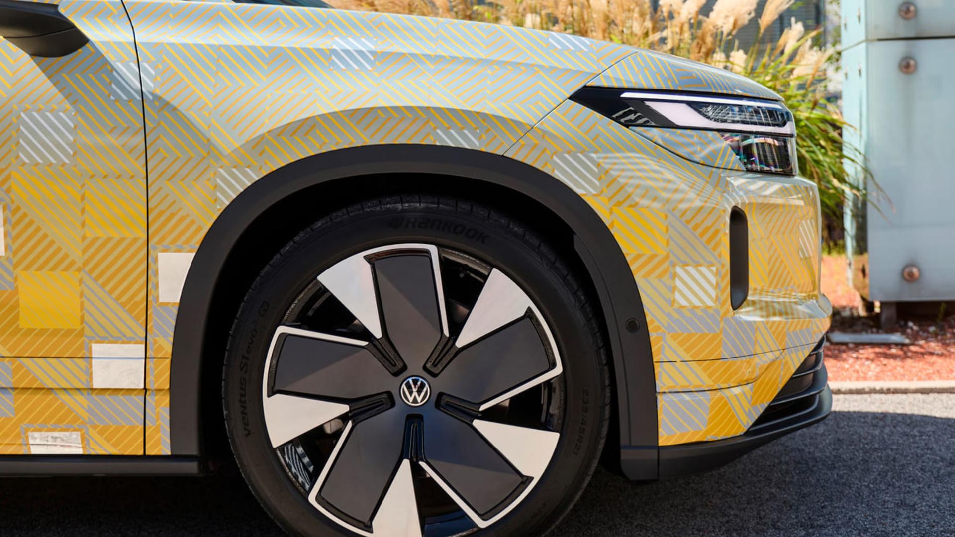 نمای نزدیک چرخ و بدنه طرح‌دار خودروی برقی فولکس‌واگن (Volkswagen) با پوشش استتار