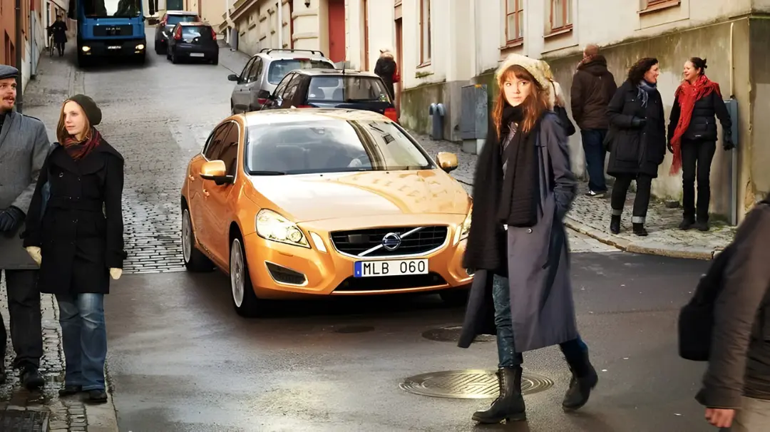 خودروی نارنجی رنگ ولوو (Volvo) در میان عابرانی که در خیابان حرکت می‌کنند