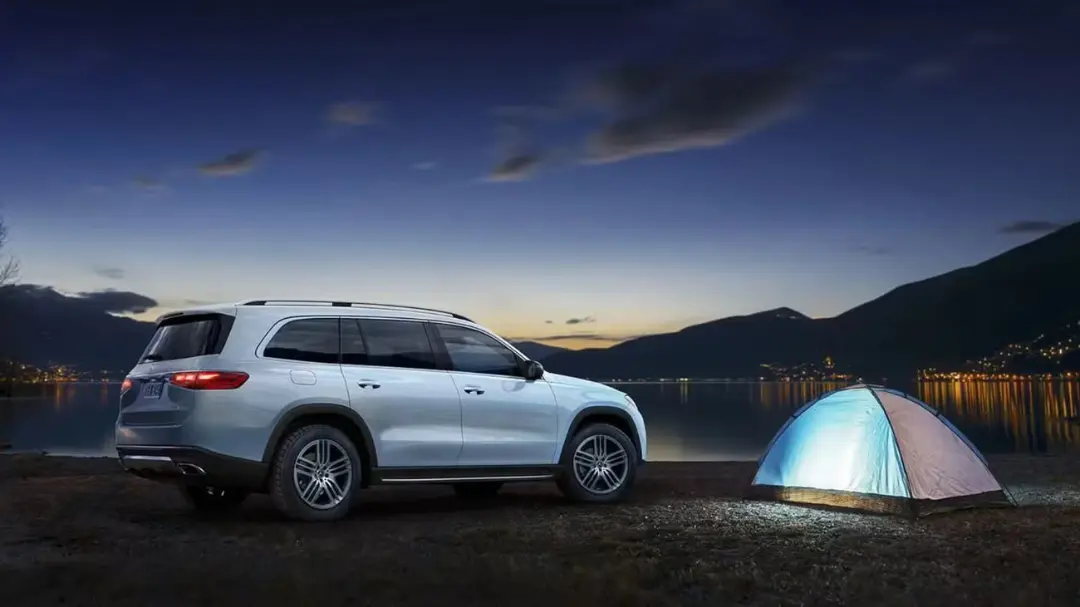 یک خودروی شاسی‌بلند mercedes gls در کنار یک چادر کمپینگ روشن در کنار دریاچه در هنگام غروب