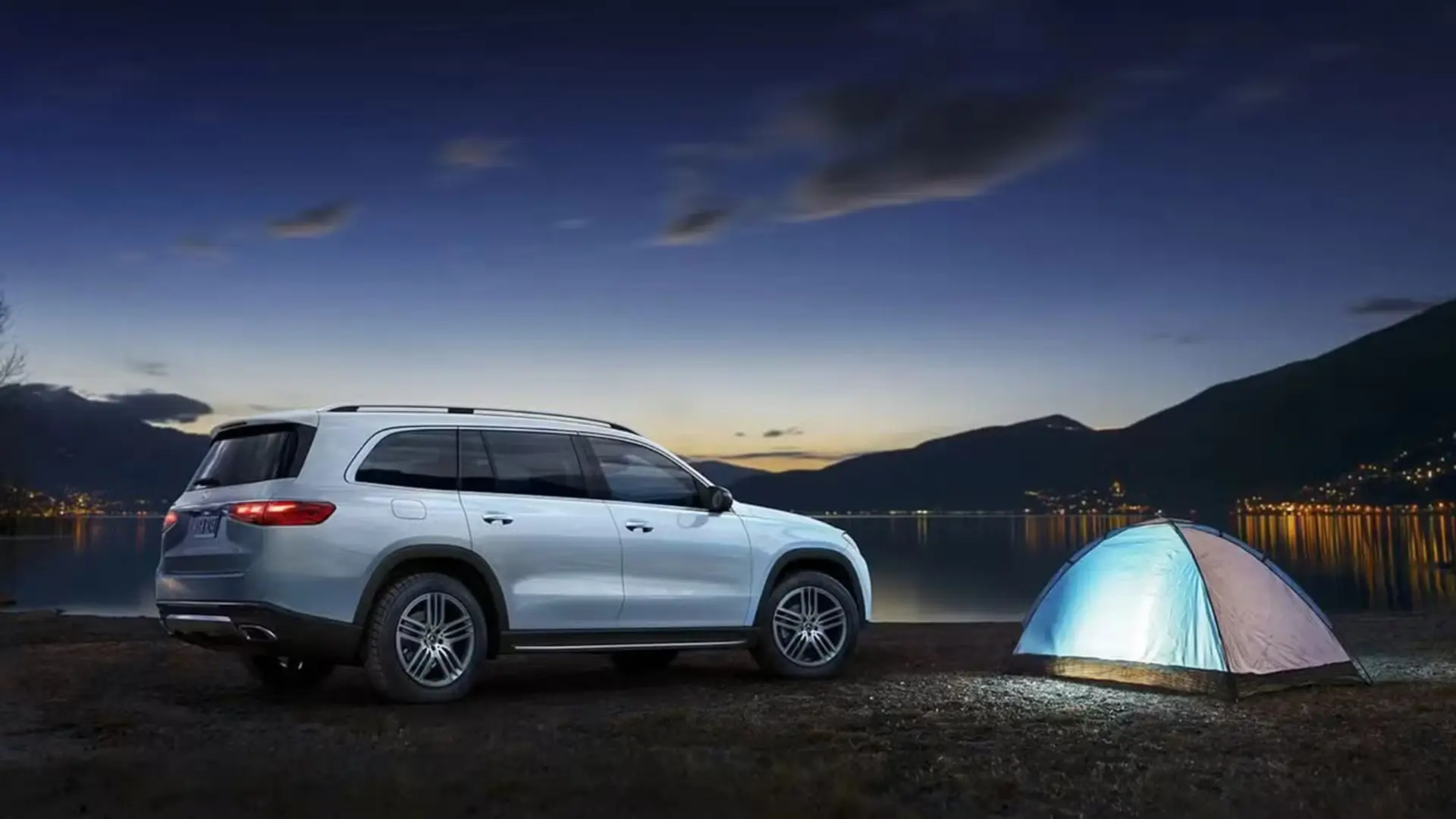 یک خودروی شاسی‌بلند mercedes gls در کنار یک چادر کمپینگ روشن در کنار دریاچه در هنگام غروب