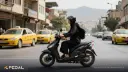 موتورسوار زن با کلاه ایمنی در حال رانندگی با اسکوتر در خیابان شهری