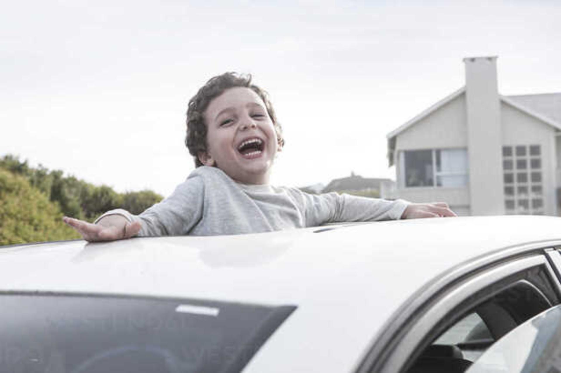 Happy boy looking through a sunroof of a car