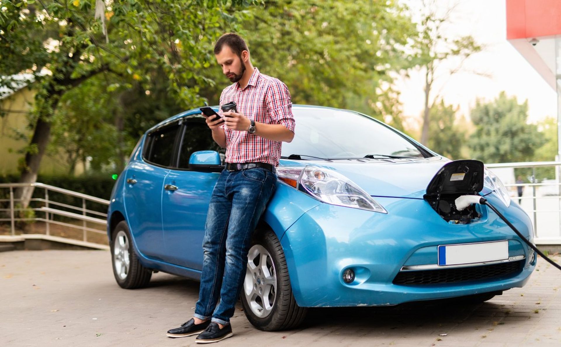 Handsome man is holding a phone while electric car charged at the charging station