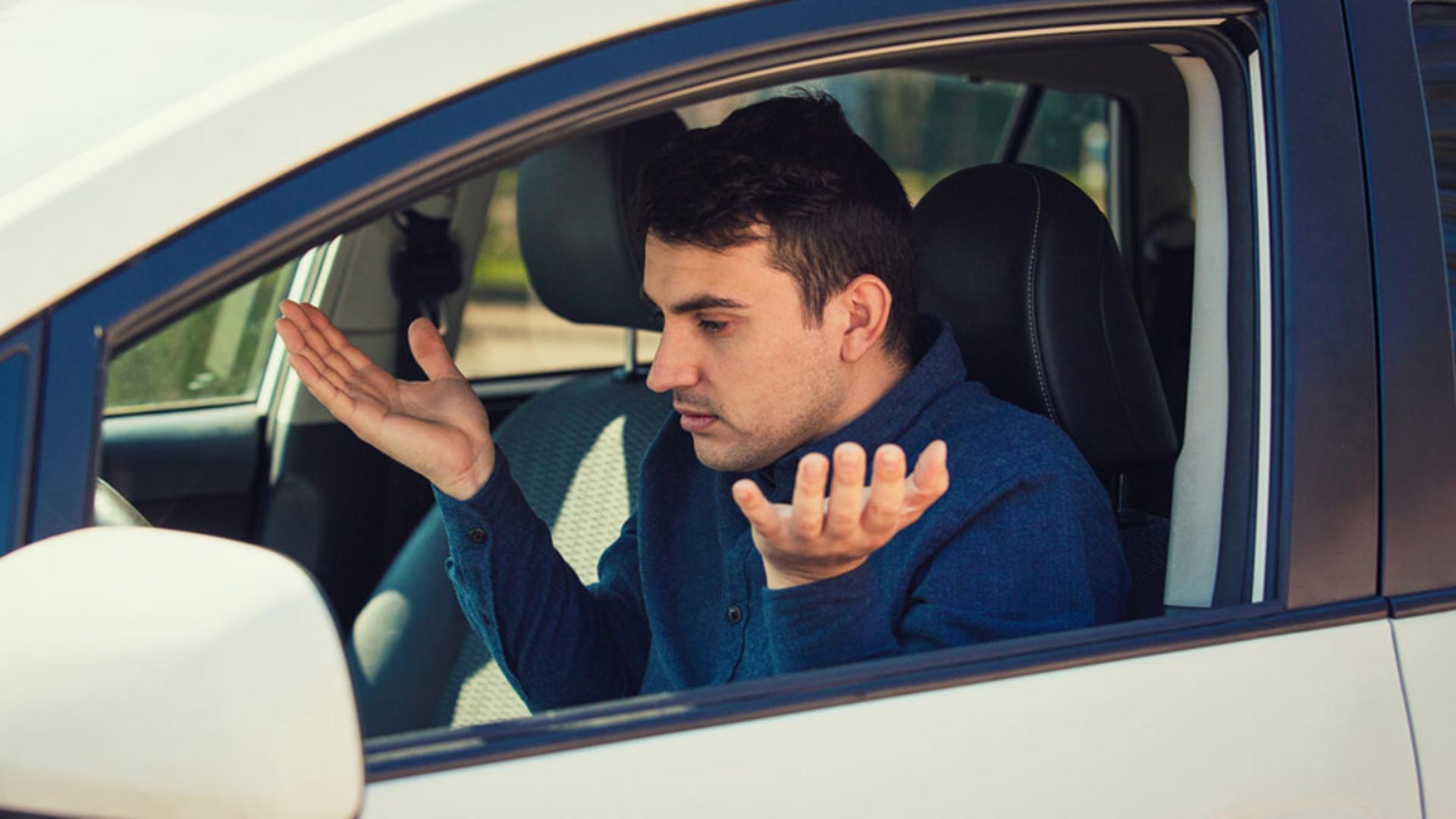 Angry young man driver, pissed off shaking hands and shrugging shoulders, has problems with the car. Displeased perplexed guy has a road accident. Traffic jam rush hour.
