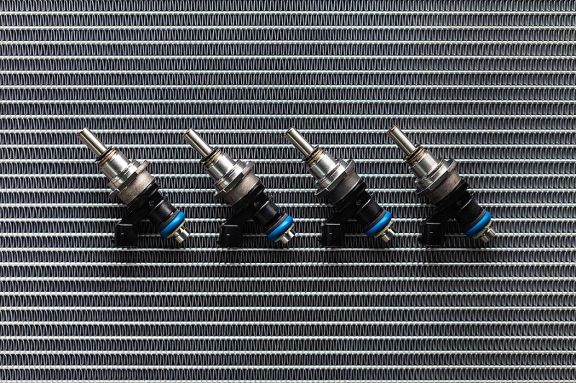 Auto Parts - four fuel nozzles of the injector for the combustion chamber of the engine lie against the background of the patterns of the cooling radiator.