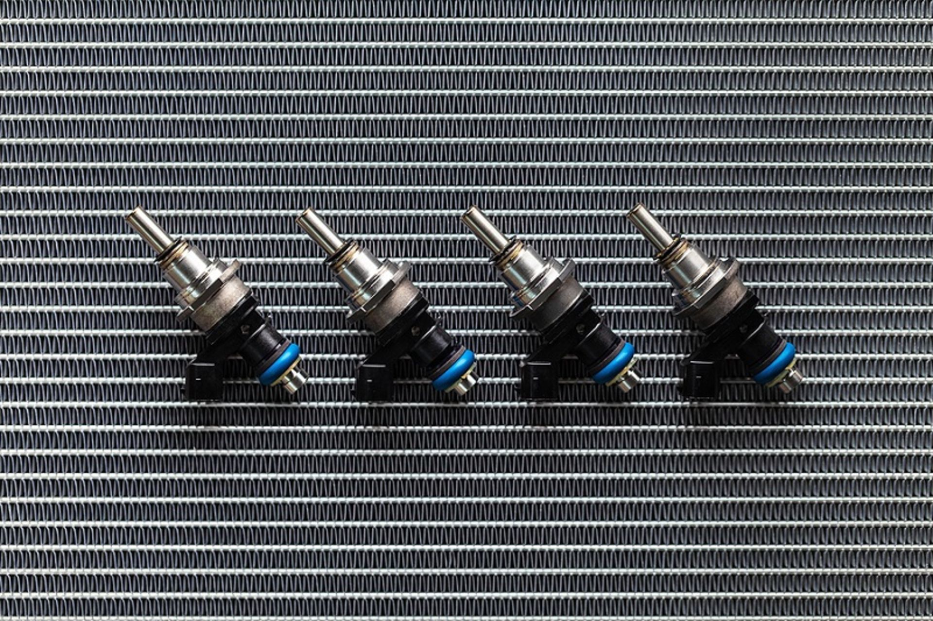 Auto Parts - four fuel nozzles of the injector for the combustion chamber of the engine lie against the background of the patterns of the cooling radiator.