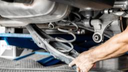 Car suspension and car mechanic service concept - Close up car suspension service with hand of mechanic man in maintenance car garage with flare light effect and copy space, use for car suspension service content