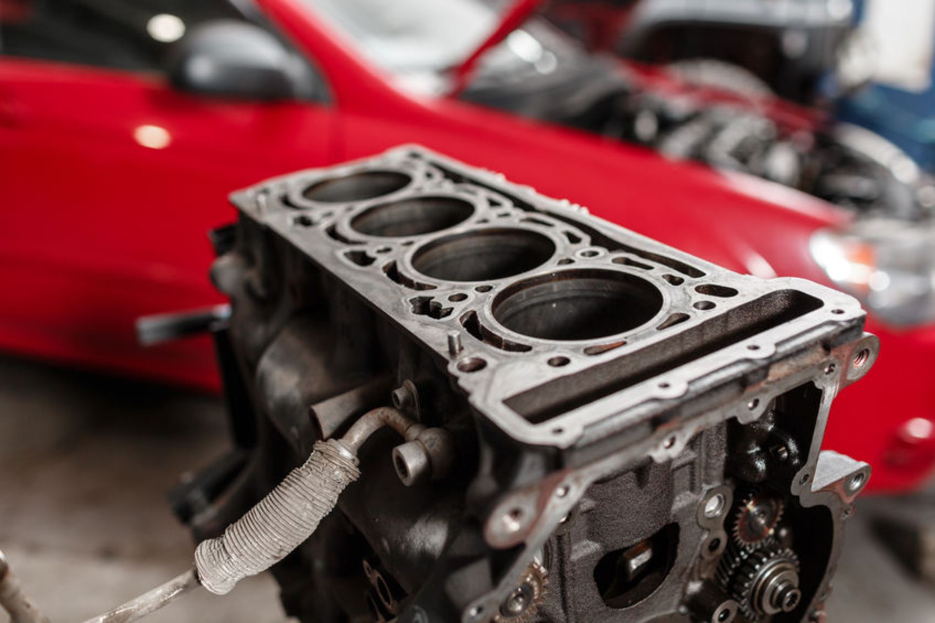 Selective focus. Engine Block on a repair stand with Piston and Connecting Rod of Automotive technology. Blurred red car on background. Interior of a car repair shop.