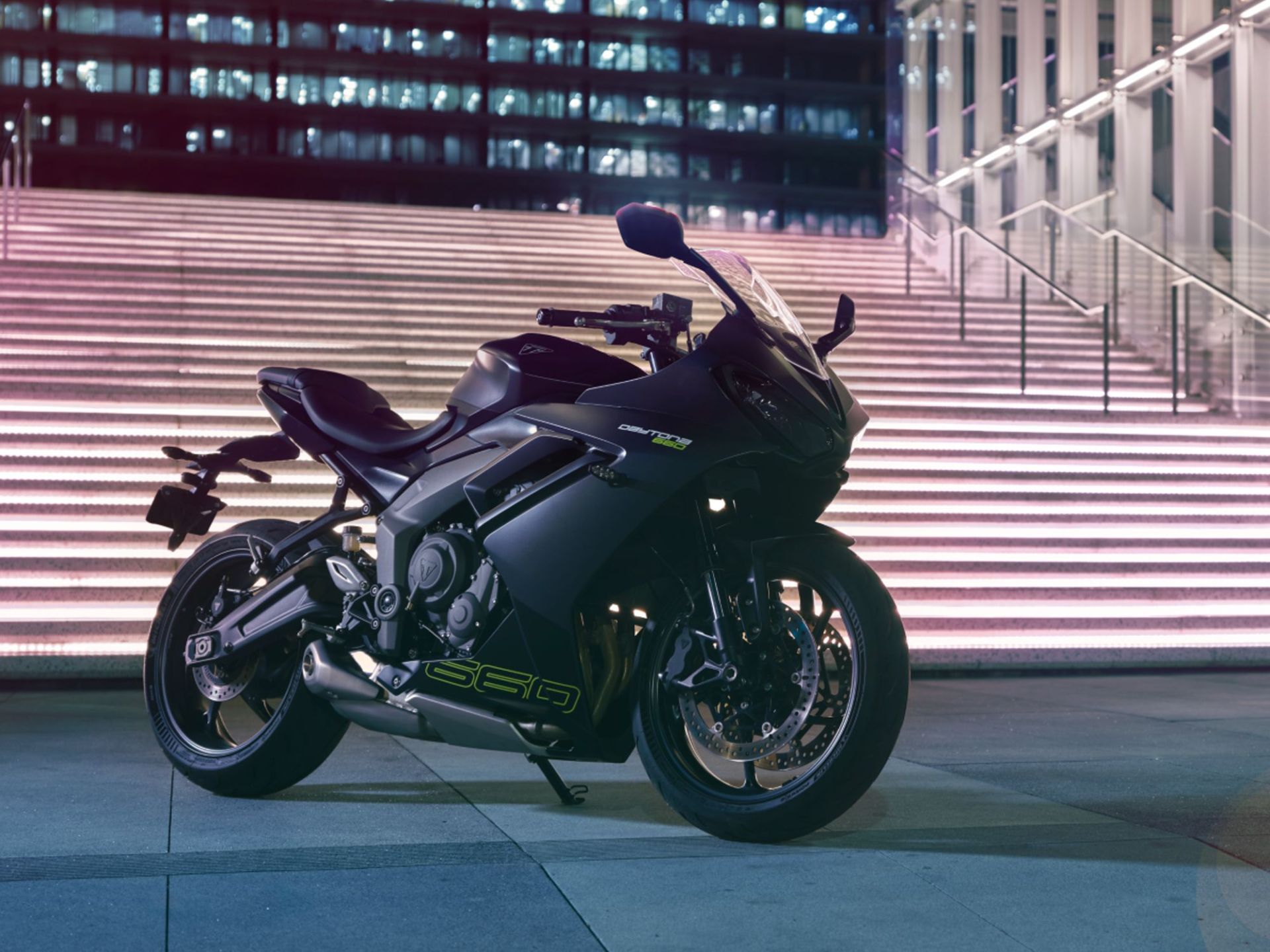 2024-Triumph-Daytona-660-parked-on-polished-concrete-at-the-foot-of-bright-stairways-with-lighted-city-buildings-in-the-background