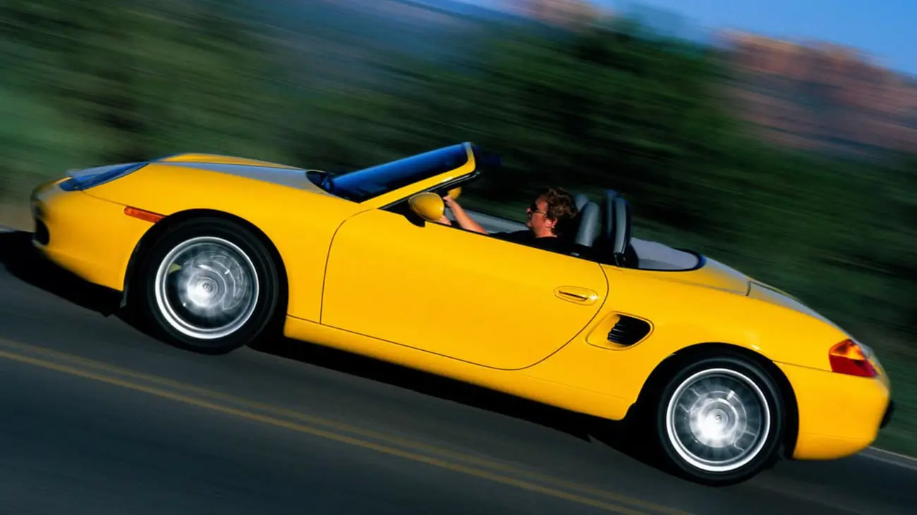 خودروی زرد پورشه باکسستر (Porsche Boxster) در حال حرکت در جاده